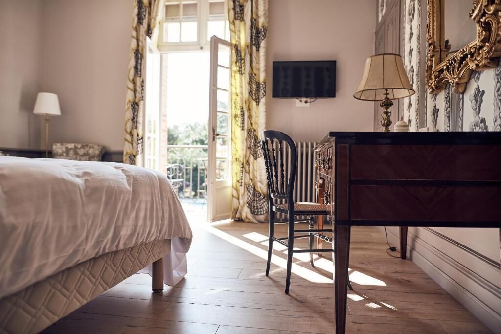 A hotel room with a bed, a desk, a chair, a TV mounted on the wall, and a view of the outdoors.