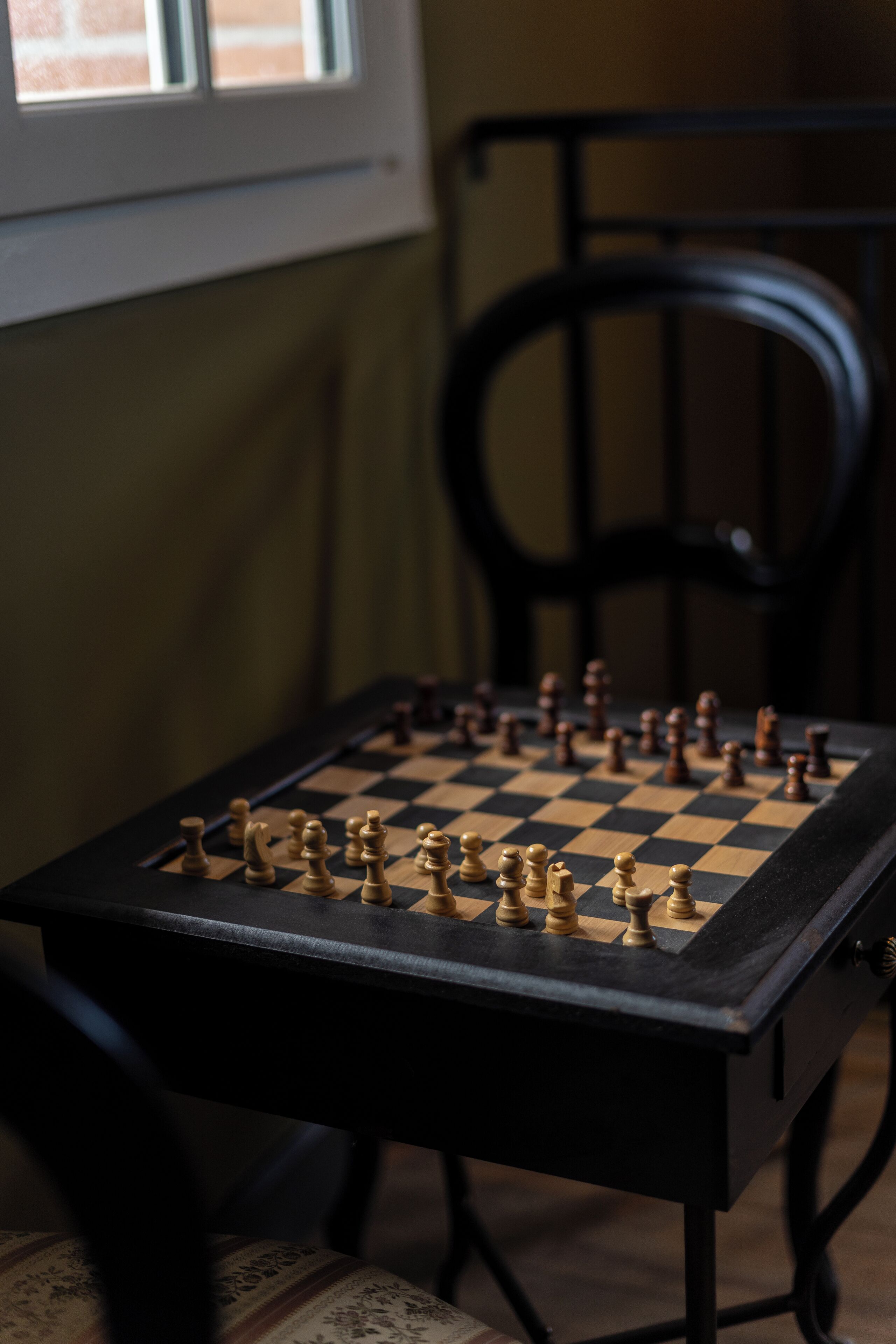 A chessboard set on a table with a chair in the background.
