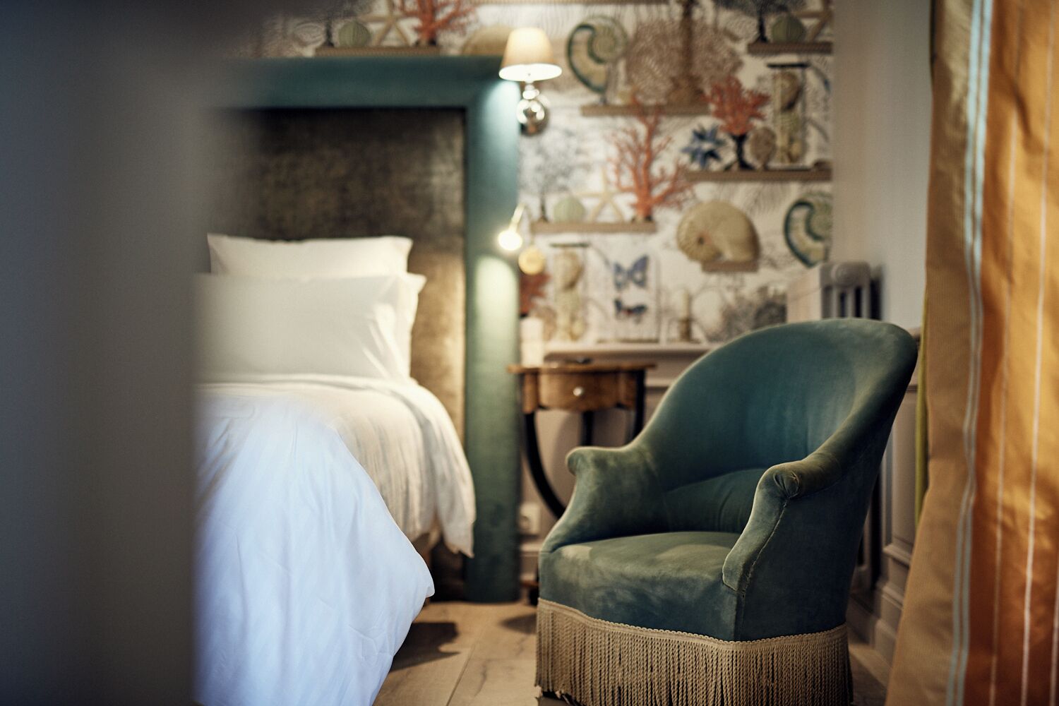 Quarto com uma cama, uma poltrona verde e uma parede decorada com conchas e arte com tema marinho.
