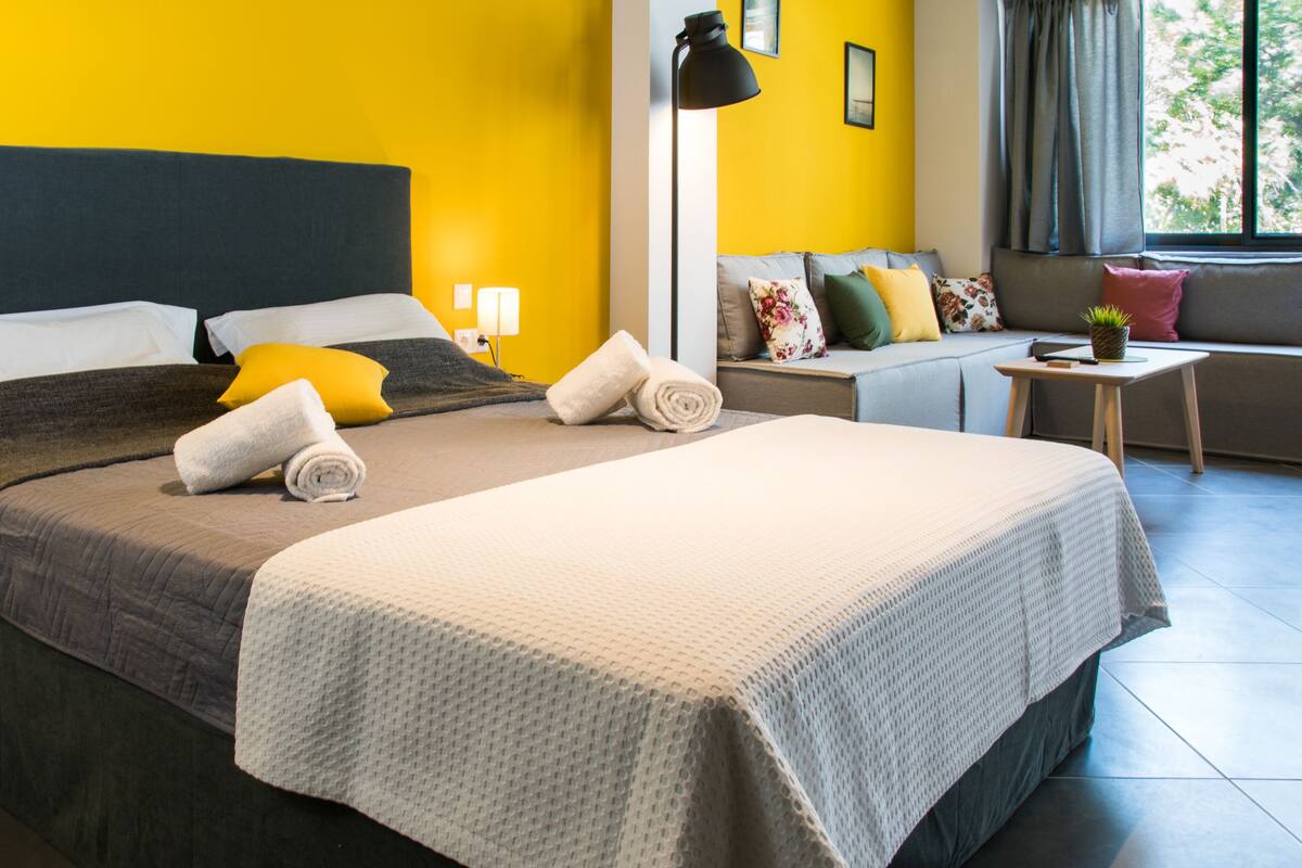 A hotel room with a large bed, a sofa, a small table, and a window with curtains.