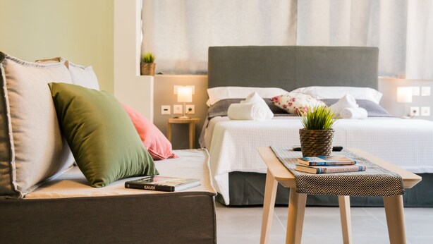 A modern hotel room with a bed, a sofa, a bedside table with a plant, and a lamp. - Eternal luxury suites (Athens)