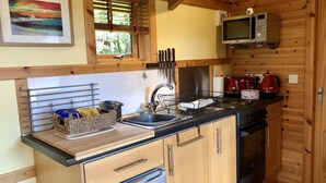 Una cocina pequeña con paredes de madera, un lavamanos, un microondas y una estufa.