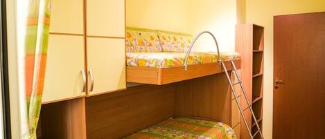 A compact bedroom with a bunk bed, a wooden wardrobe, a ladder, and a small desk.