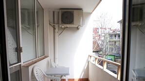 A balcony with a table and chairs, air conditioning unit, and a view of buildings. - Apartment Geo Milev (Plovdiv)