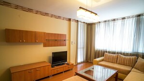 A living room with a sofa, ottoman, TV stand, and wooden cabinets. - Apartment Geo Milev (Plovdiv)