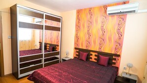 A bedroom with a large bed, a wardrobe with multiple shelves, a nightstand, and a wall-mounted air conditioner. - Apartment Geo Milev (Plovdiv)
