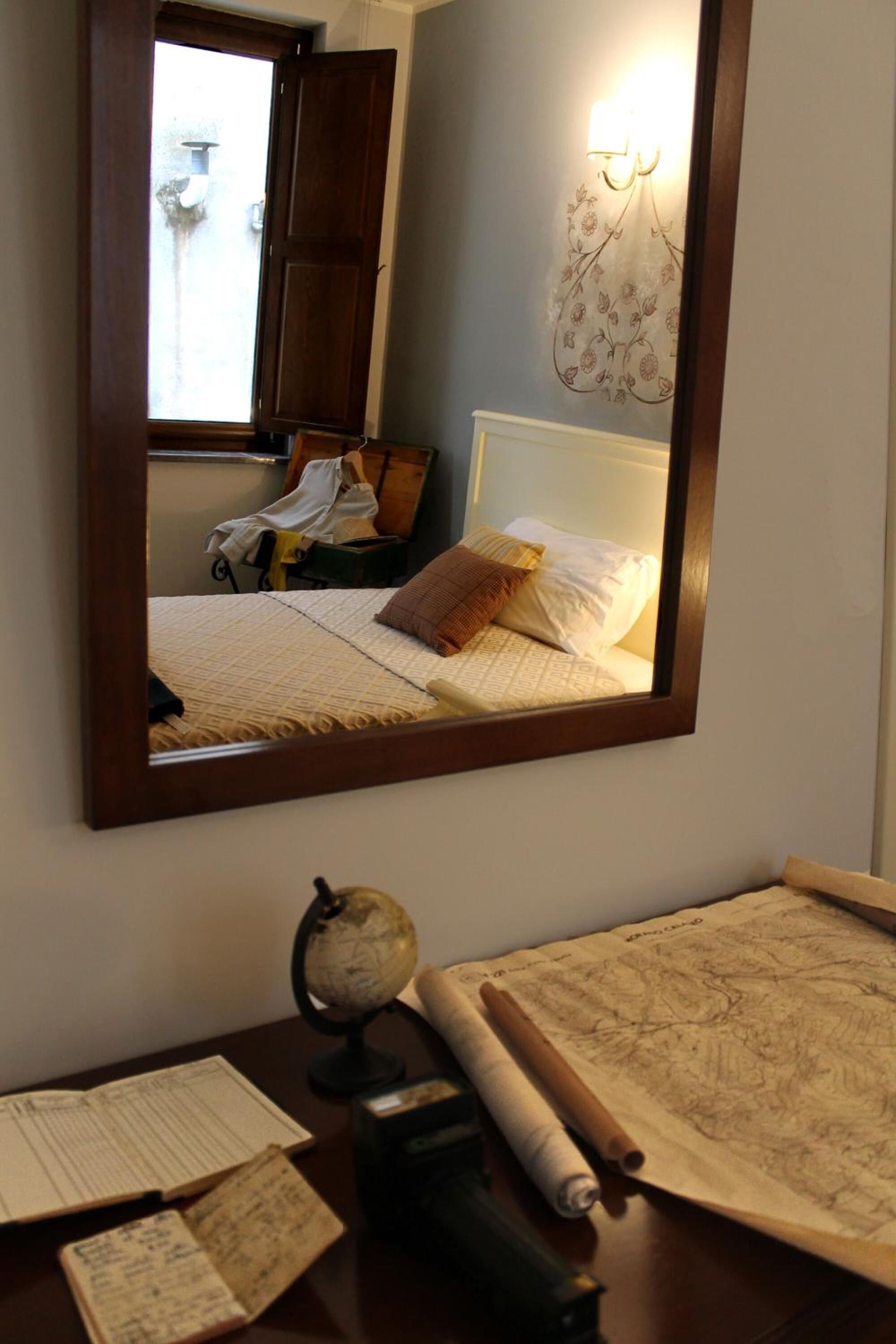 Une chambre avec un grand miroir, un lit avec des oreillers, un globe terrestre et une carte sur la table.