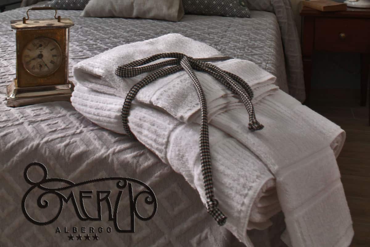 A neatly made bed with a clock, pillows, and a folded towel.