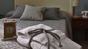Een opgemaakt bed met een klok, kussens en een gevouwen handdoek.