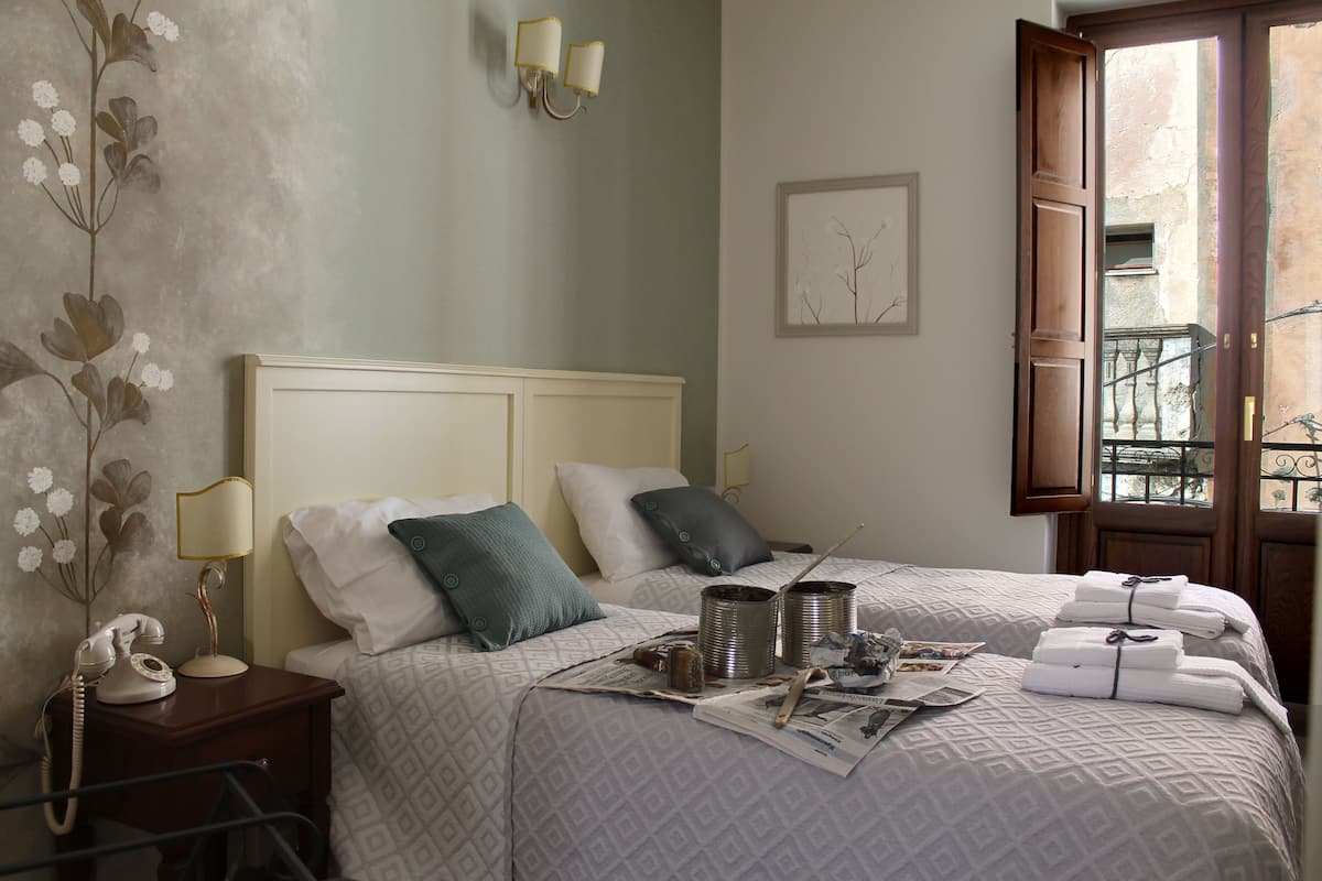 A bedroom with a bed, pillows, a nightstand with a lamp, a framed picture, and a window with a view.