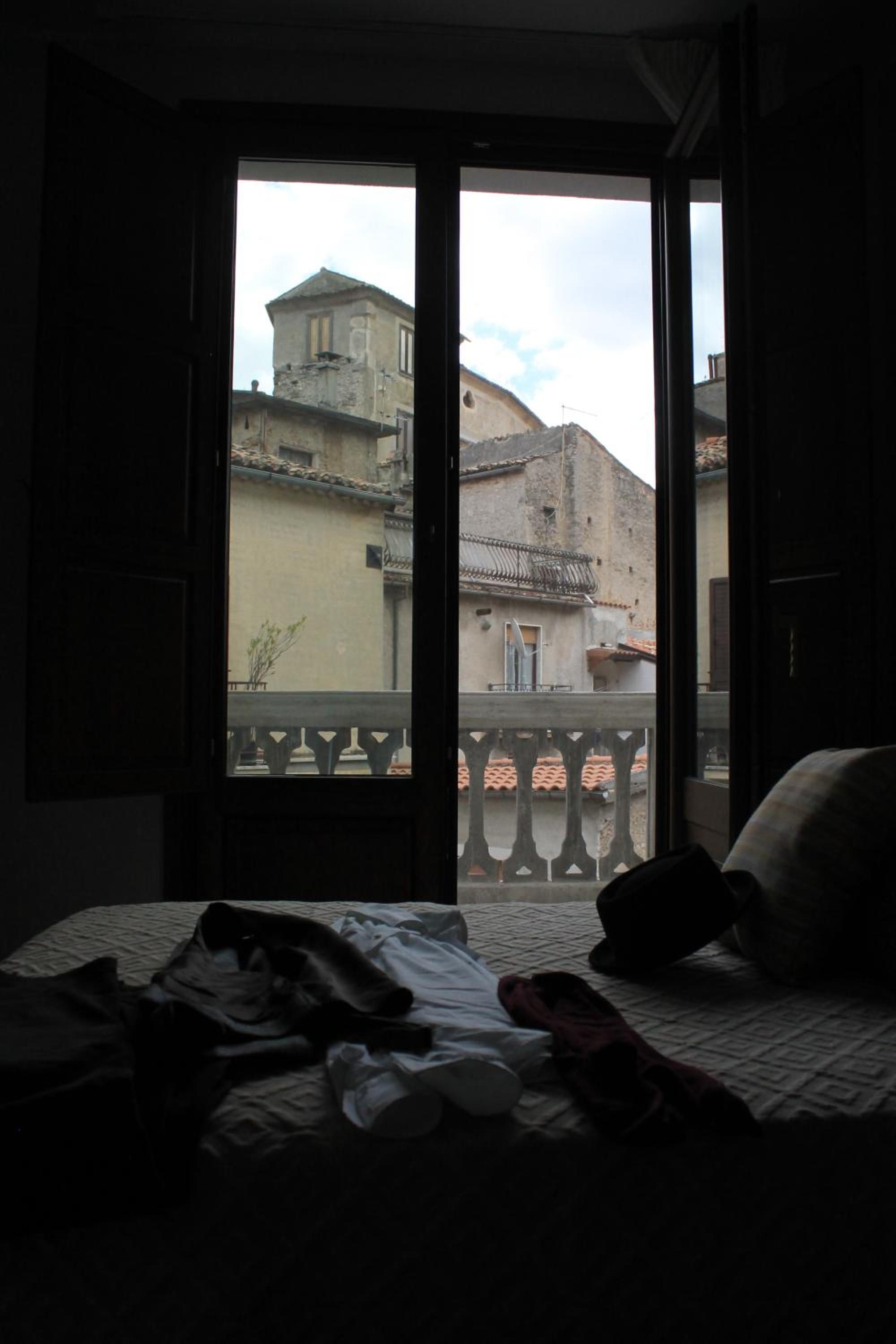 A room with an open door leading to a balcony with a view of old buildings.
