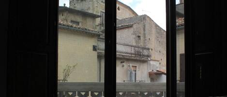 A room with an open door leading to a balcony with a view of old buildings.