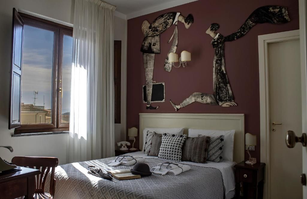 A bedroom with a bed, bedside tables, a window, and a view of buildings outside.