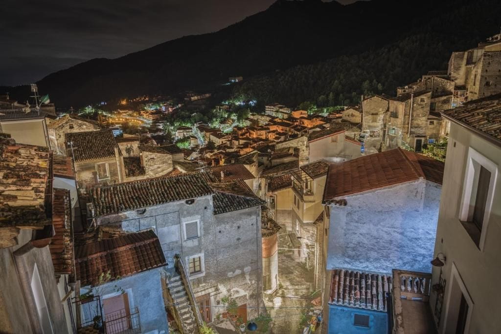 A narrow street in a historic town with old buildings and a mountain in the background.