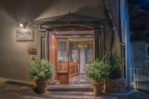 Una entrada de edificio con puerta de vidrio, plantas en macetas y una reja decorativa.