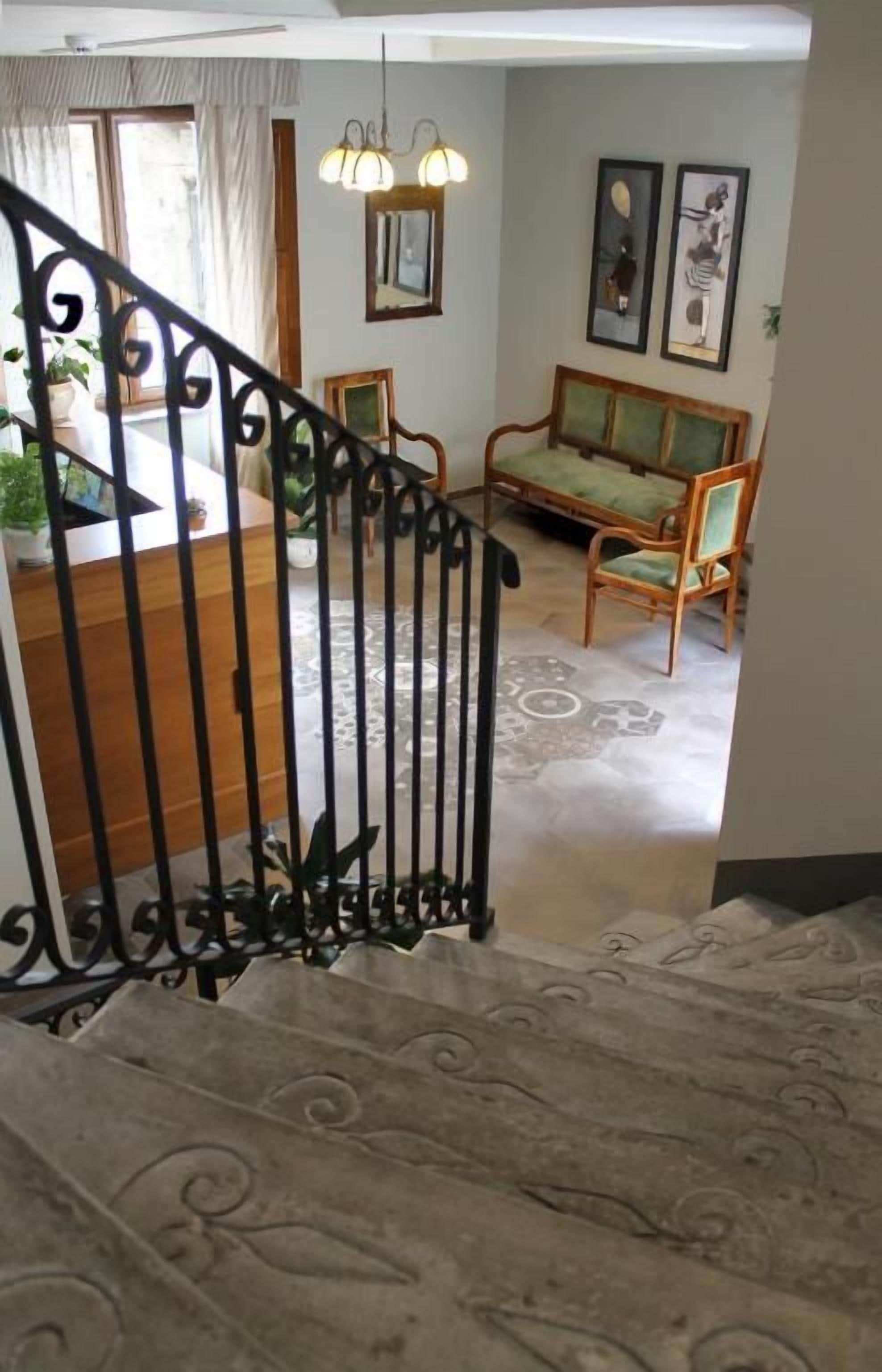 Un escalier orné de balustres menant à un espace de vie comprenant un canapé, des fauteuils et une table à manger.