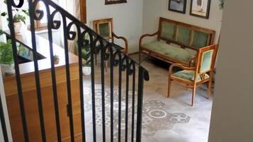 Un escalier orné de balustres menant à un espace de vie comprenant un canapé, des fauteuils et une table à manger.