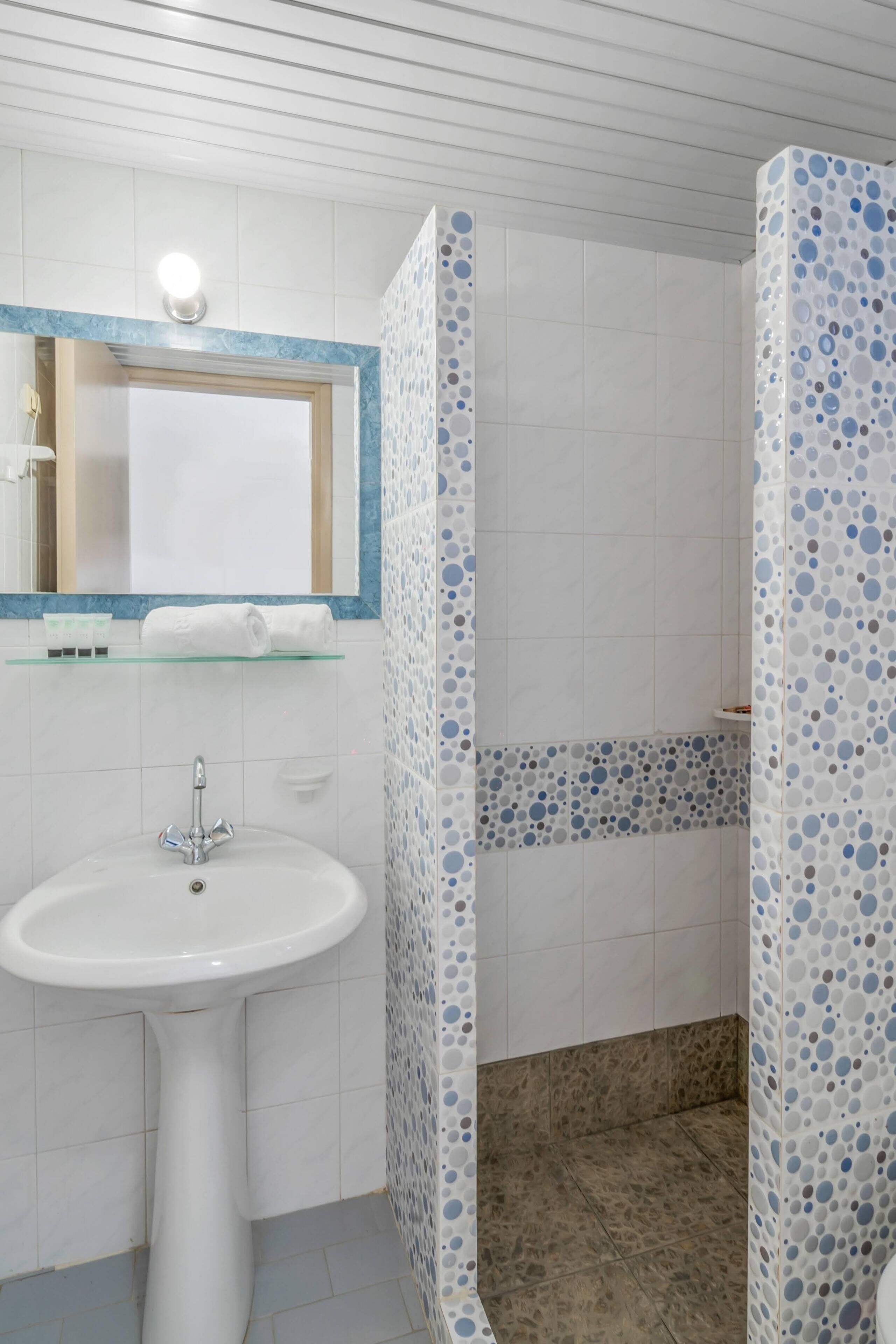 A bathroom with a white sink, a mirror, and a shower area with blue and white patterned tiles.