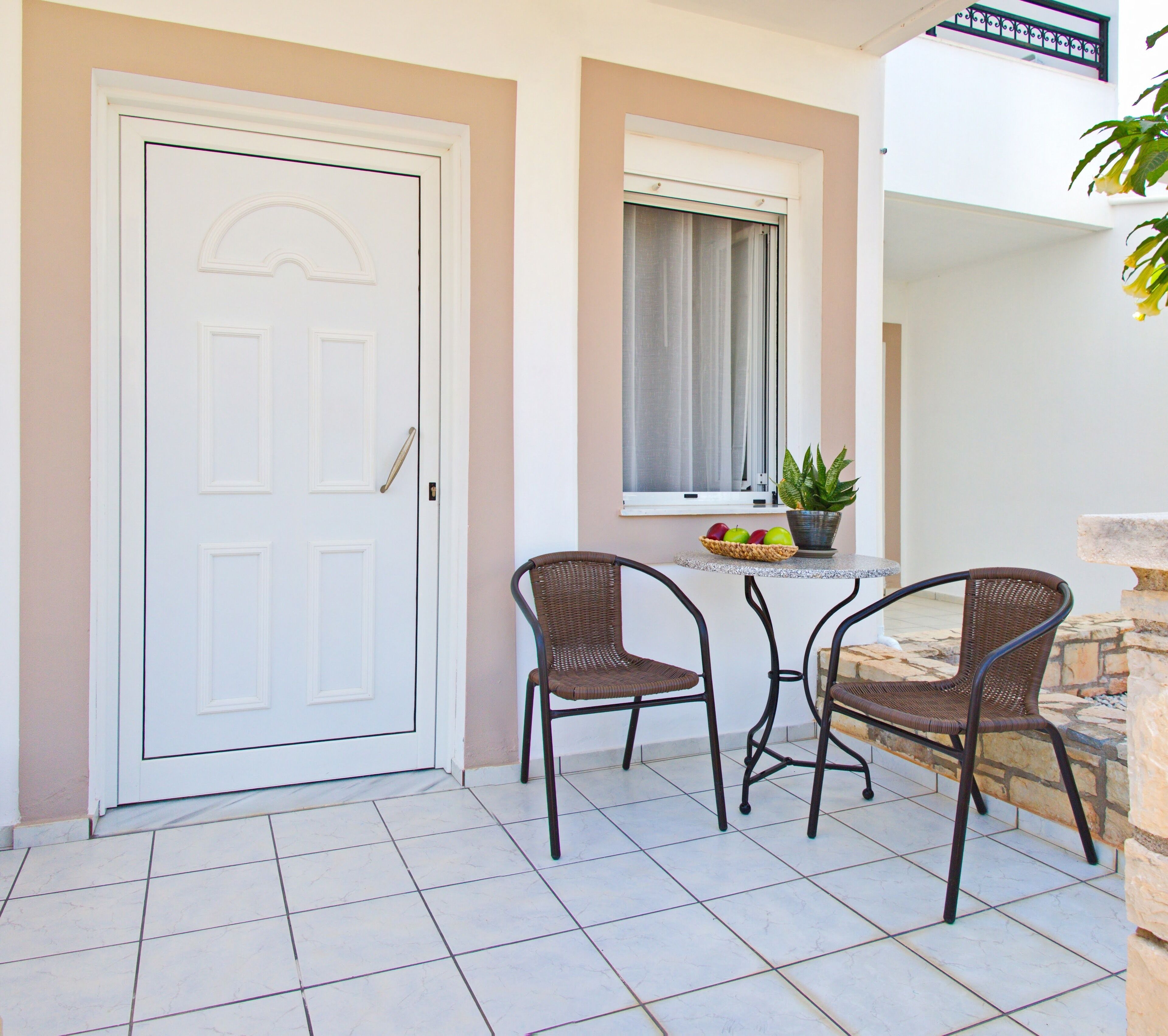 A white door with a handle, two wicker chairs, a small table with a fruit bowl, and a potted plant.