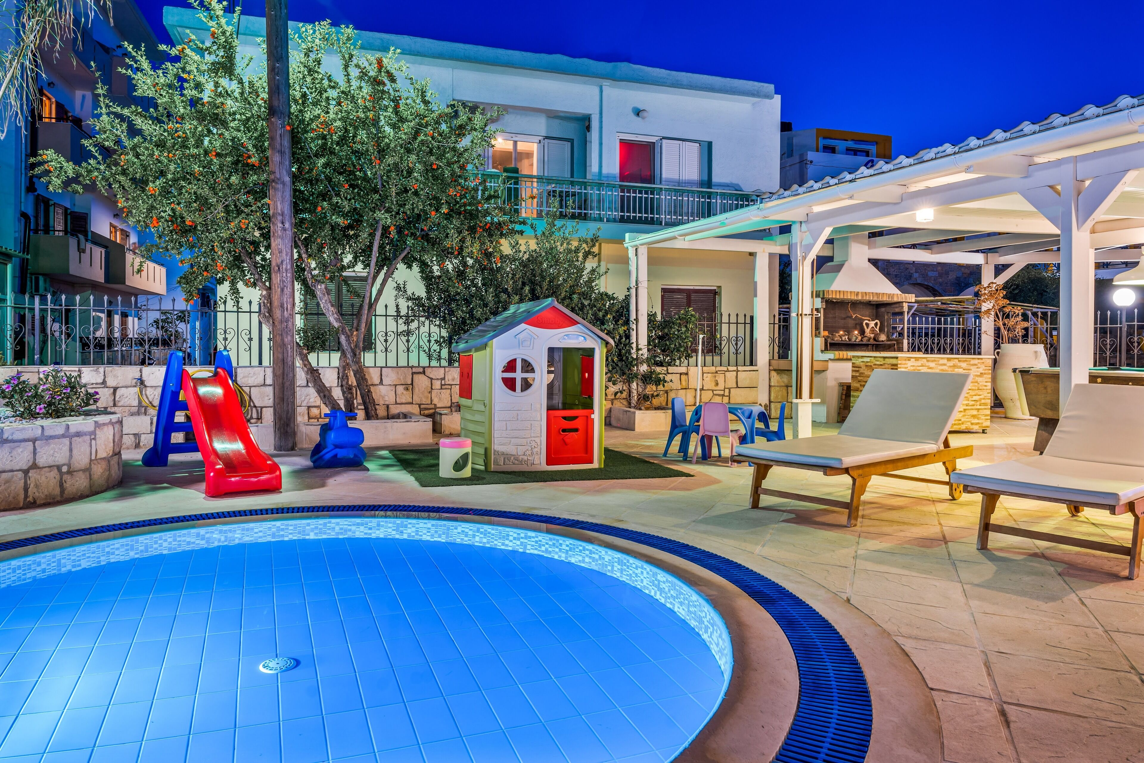 A swimming pool with a slide, a small playhouse, lounge chairs, and a covered patio area.