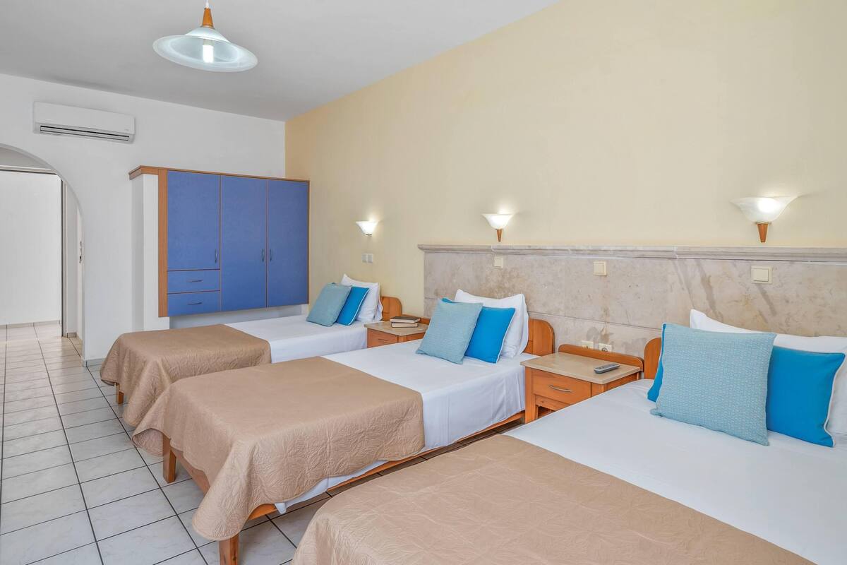 A hotel room with two beds, a wardrobe, and a nightstand with a lamp.