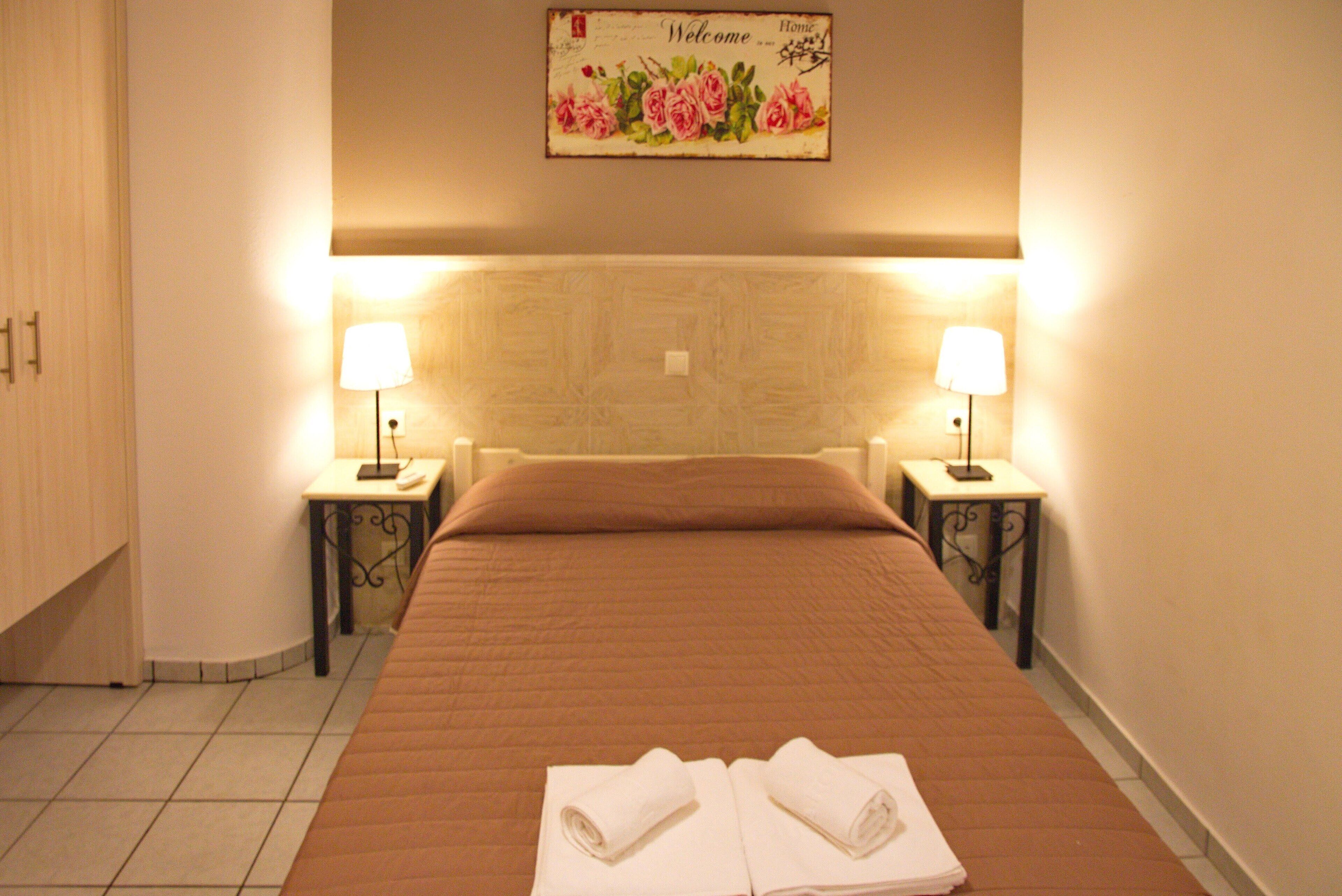 Una habitación de hotel con una cama, dos lámparas de noche, un cartel de bienvenida y dos toallas sobre la cama.