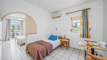 Une chambre d’hôtel avec un lit, une petite table sur laquelle se trouvent une tasse et des pâtisseries, une chaise, une fenêtre avec des rideaux et un appareil de climatisation.