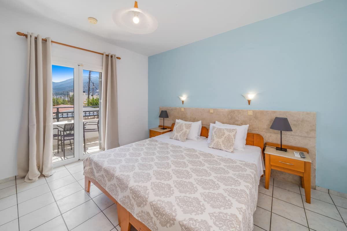 A bedroom with a bed, two bedside tables, a nightstand, a balcony with a view, and a ceiling light.