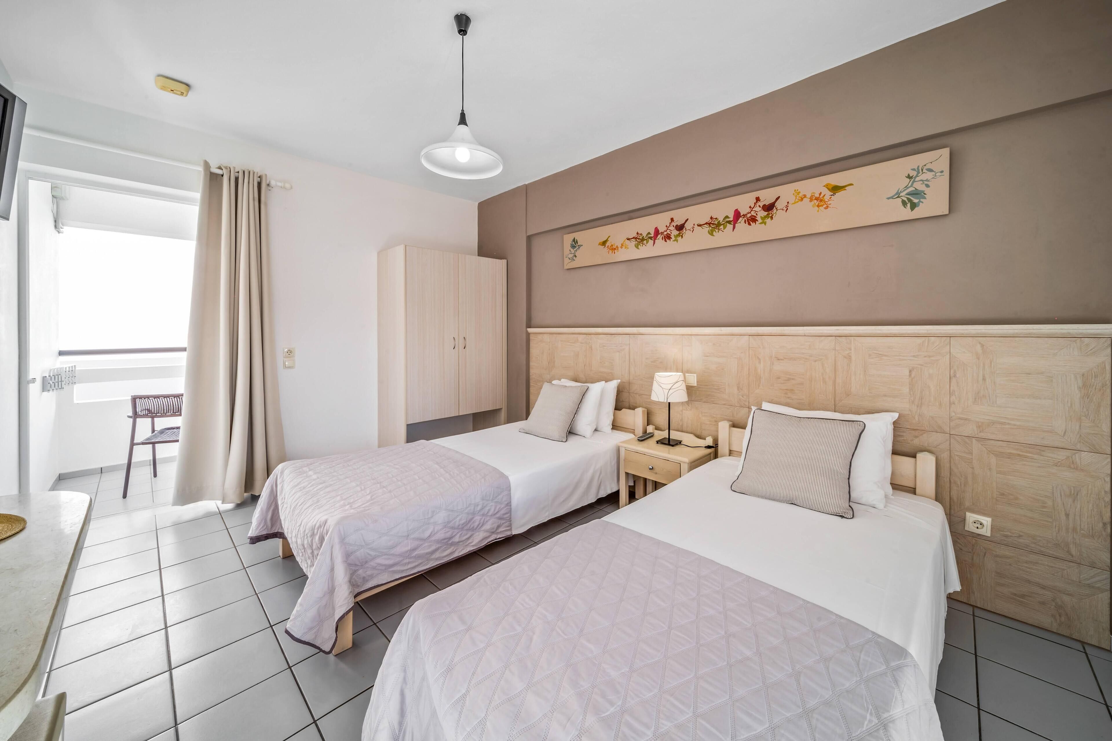 A hotel room with two beds, a desk, a chair, and a window with curtains.