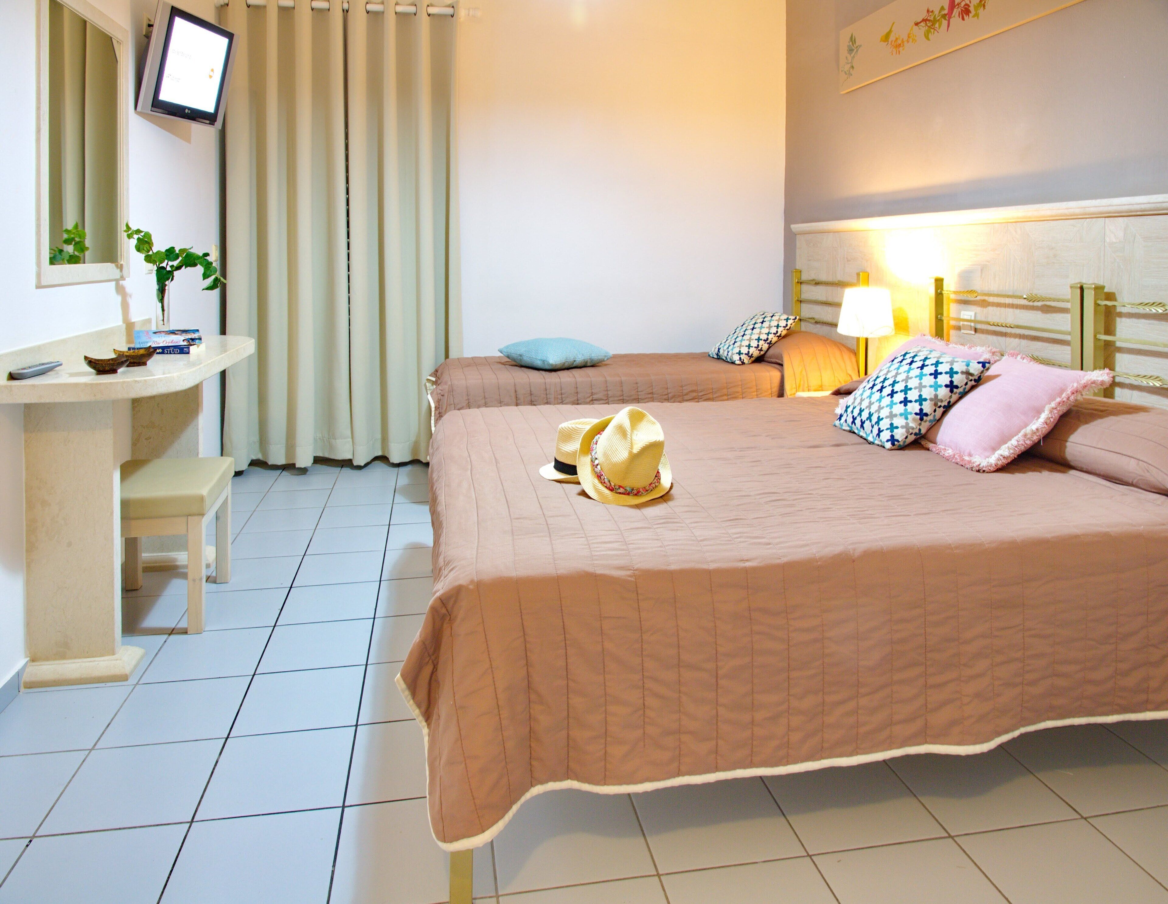A hotel room with two beds, a desk, a chair, a TV, and a lamp.