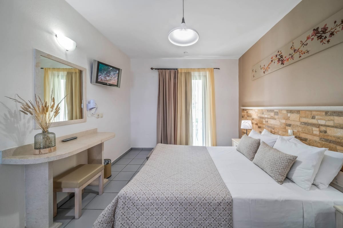 A hotel room with a bed, bedside table, mirror, and a wall-mounted TV.