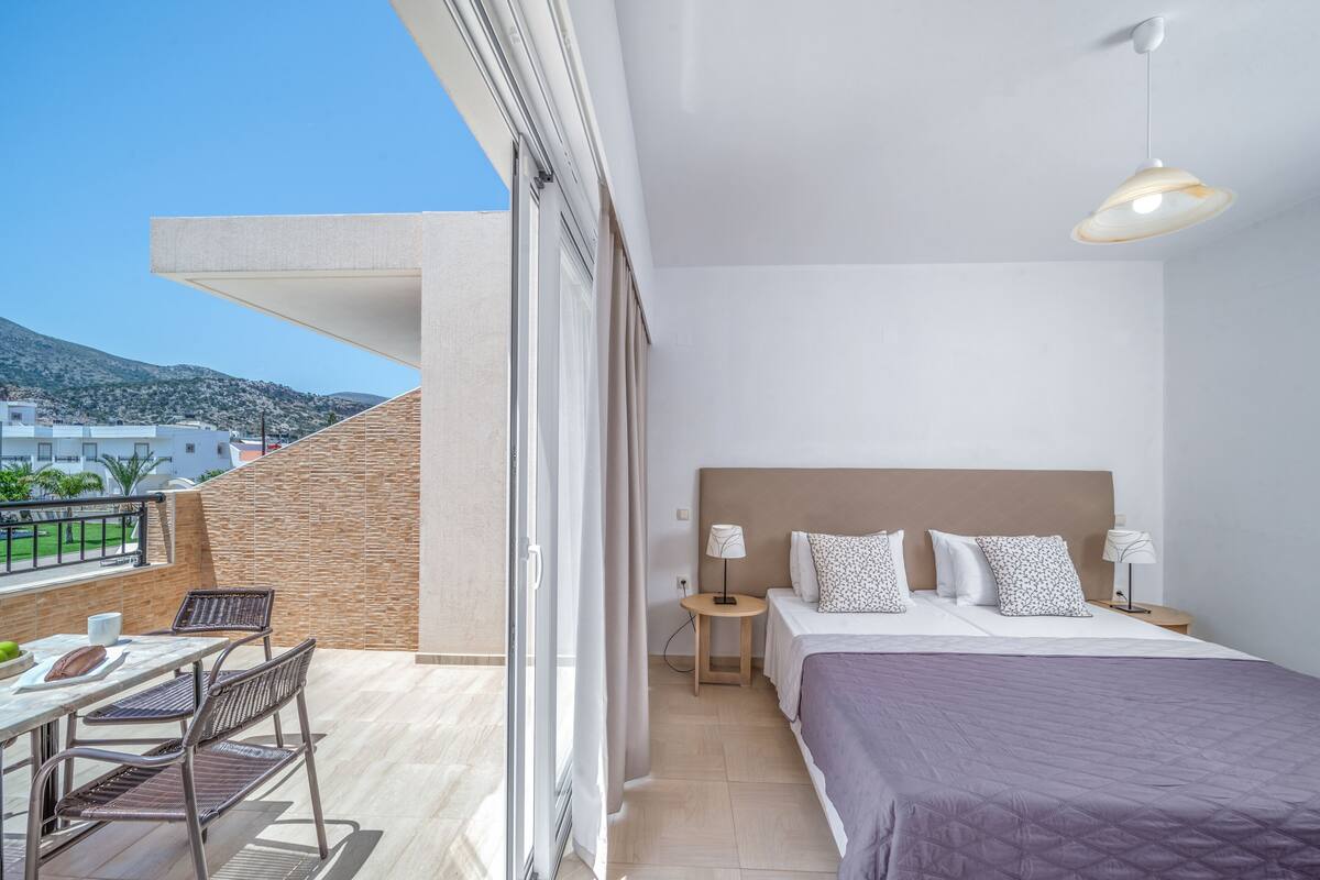 A modern hotel room with a balcony, a bed with a headboard, two bedside tables with lamps, and a view of the cityscape.