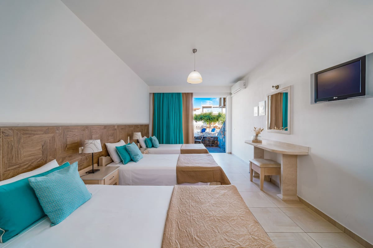 A hotel room with two beds, a TV, a desk, and a view of the outside.