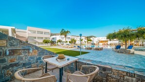 A patio area with wicker chairs and a table, overlooking a pool and lounge chairs. - Maria Rousse (Hersonissos)