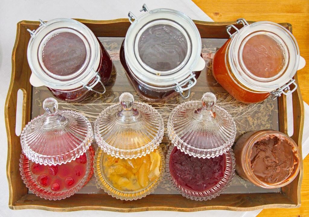 A tray with three glass jars and four glass containers with lids, likely containing preserved fruits or jams.