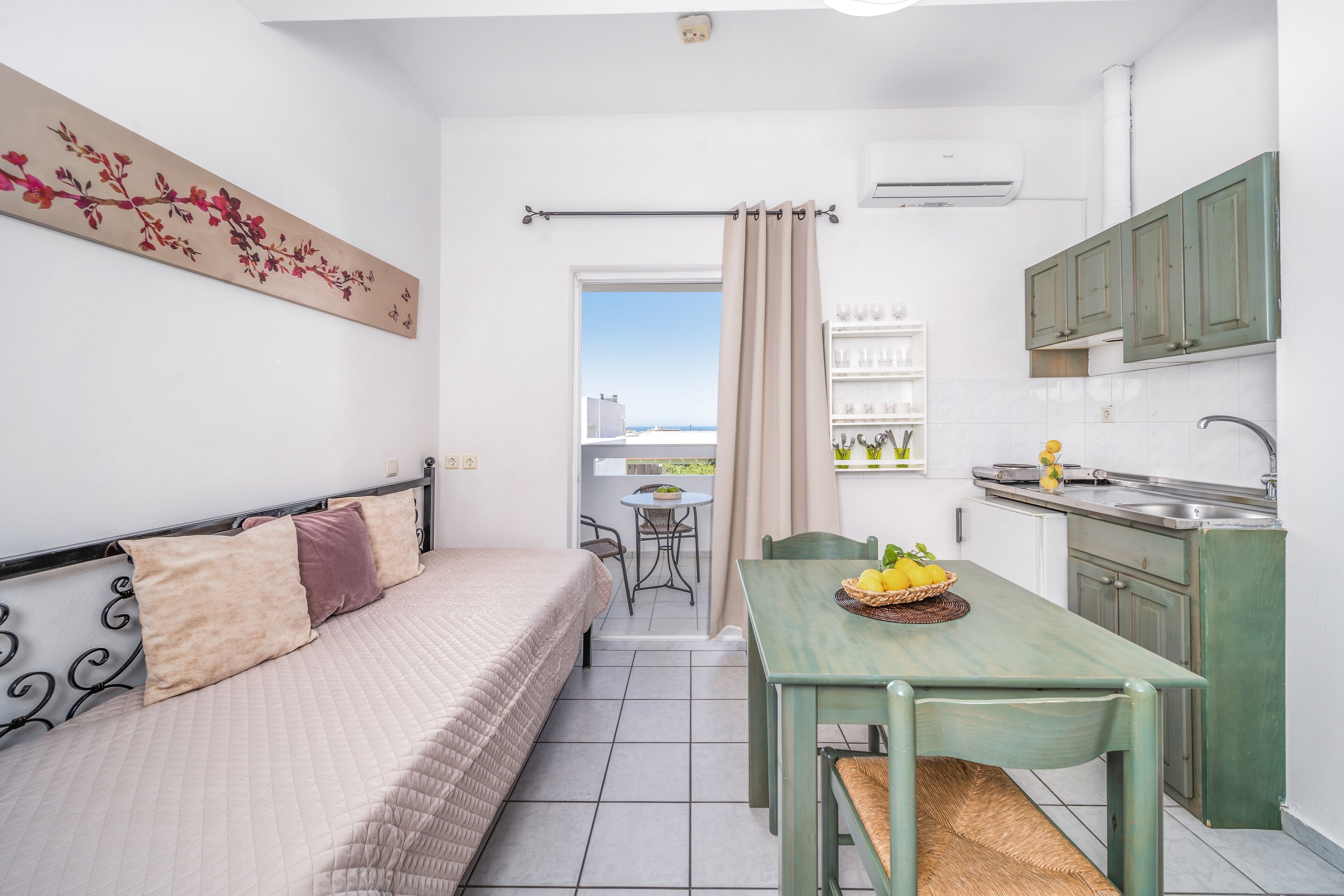 Une pièce de taille modeste comprenant un lit, une table à manger avec des chaises, un coin cuisine et une vue par une porte.