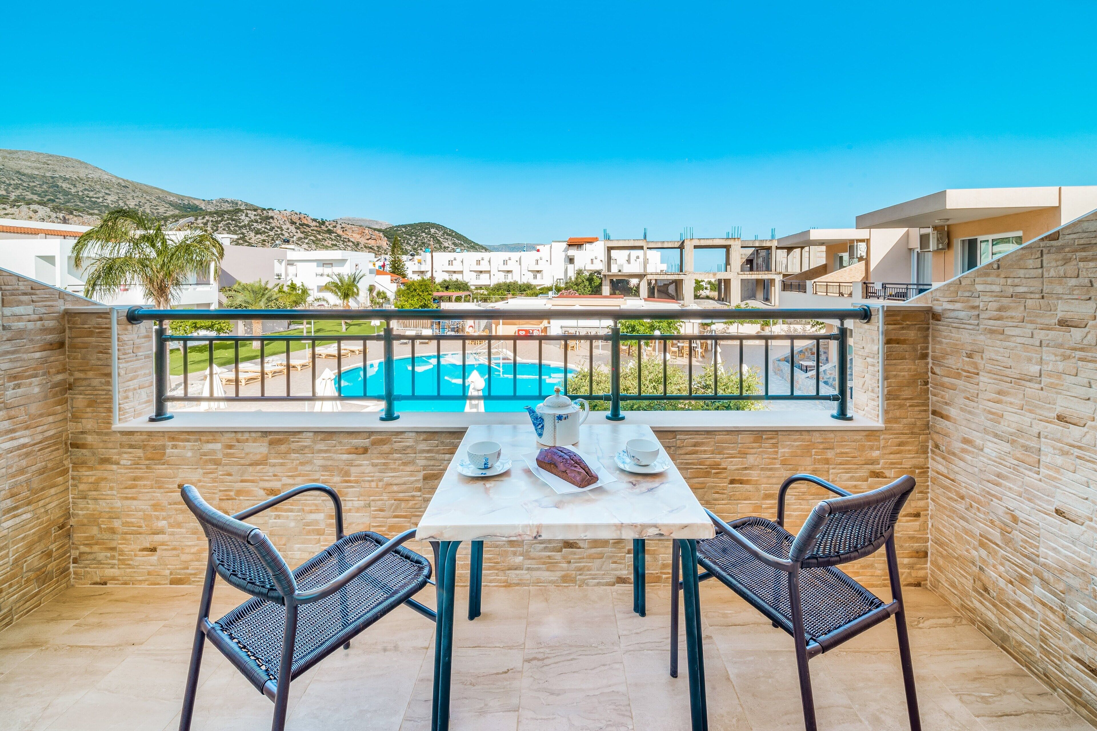 Un balcón con mesa y sillas, con vista a una piscina y edificios.