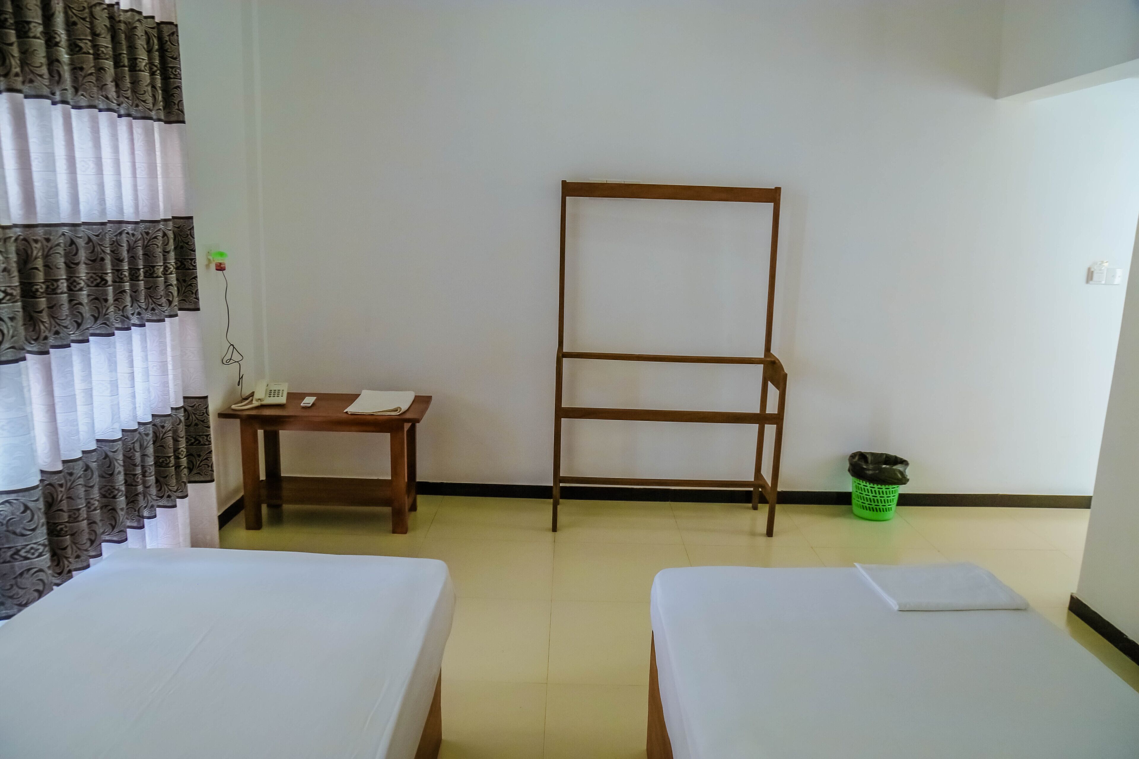 Une chambre d'hôtel avec deux lits, une étagère en bois, une petite table avec un téléphone et un panier à linge vert.