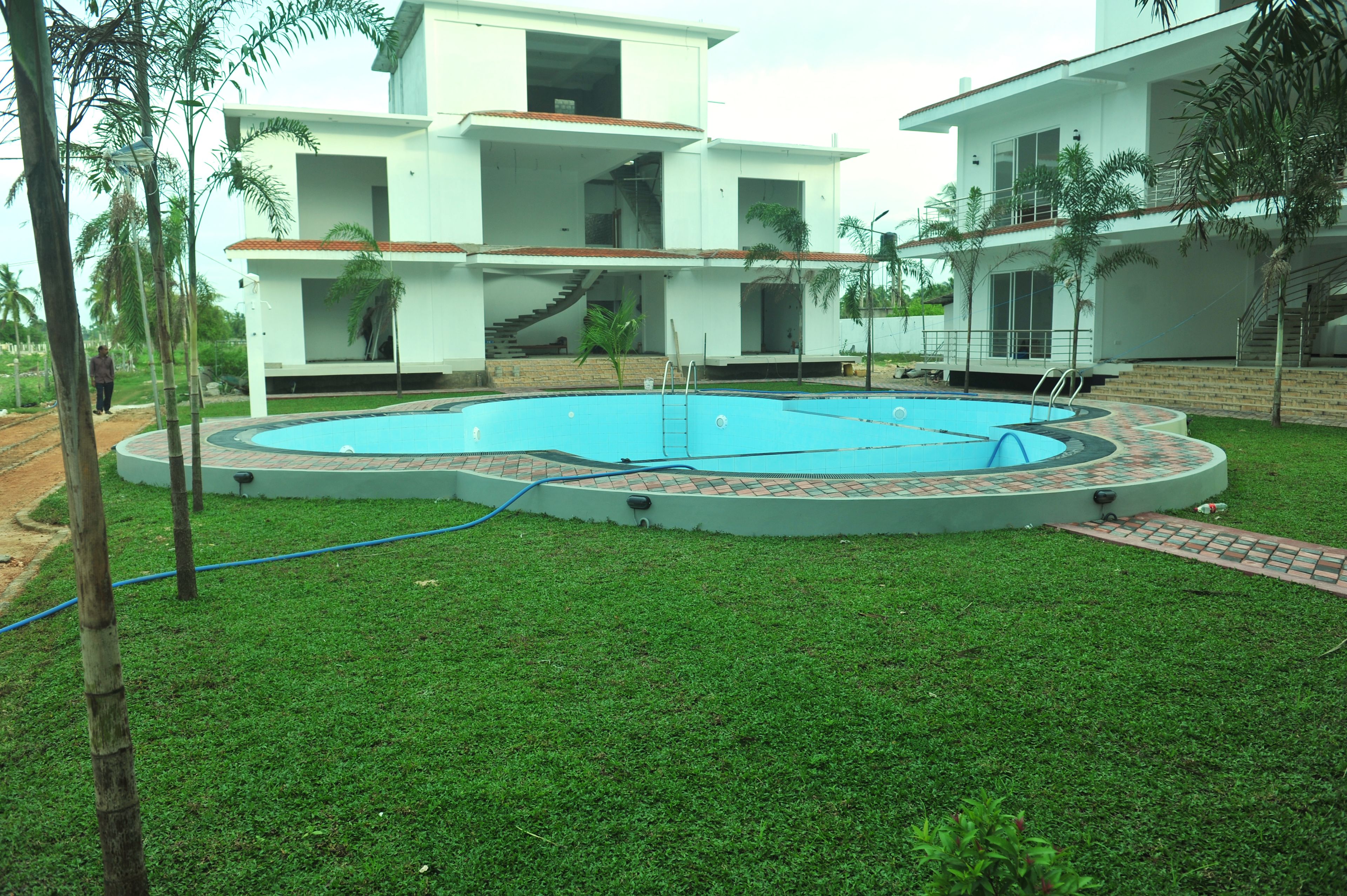 A modern two-story house with a swimming pool, surrounded by well-maintained grass and palm trees.