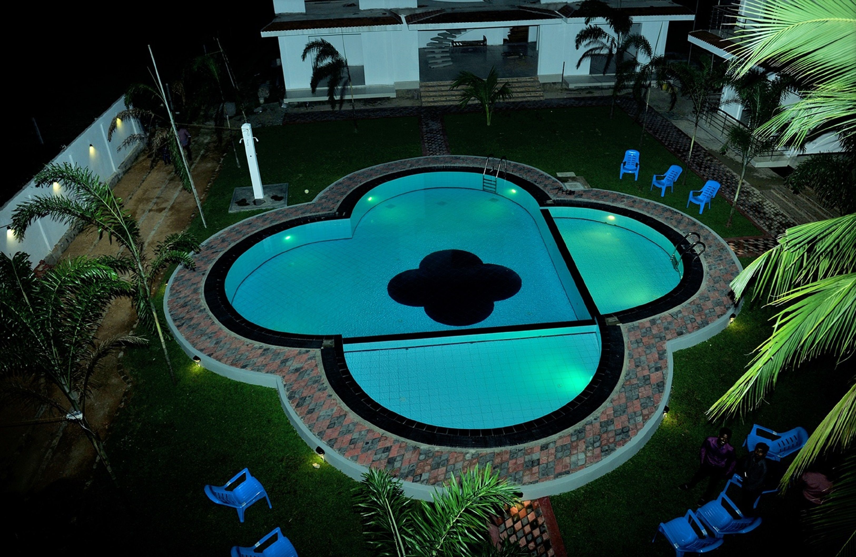 Une piscine au design original, en forme de fleur, entourée d’une bordure en briques et agrémentée de chaises bleues.