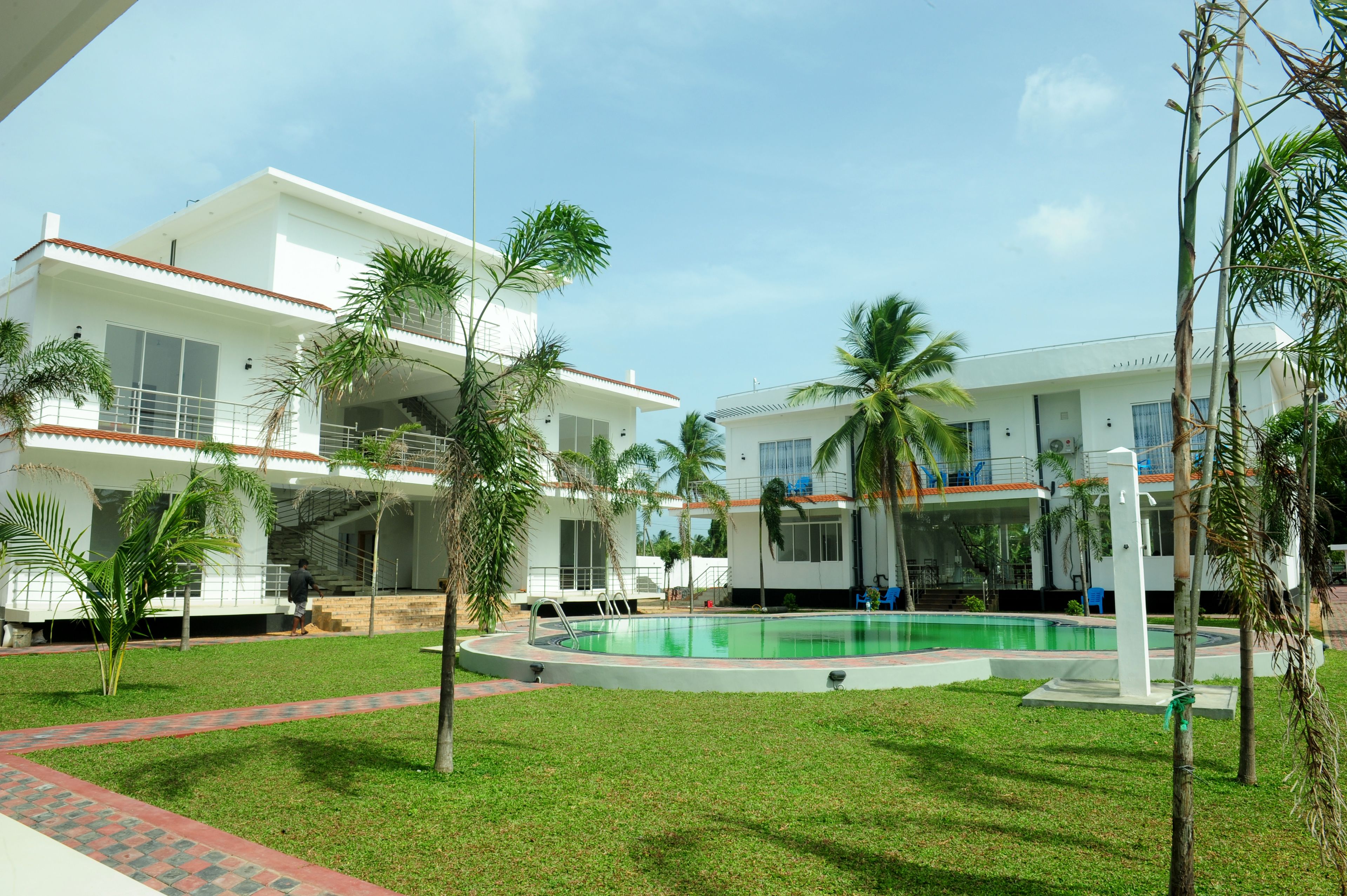 A modern hotel with a swimming pool, surrounded by palm trees and a well-maintained lawn.