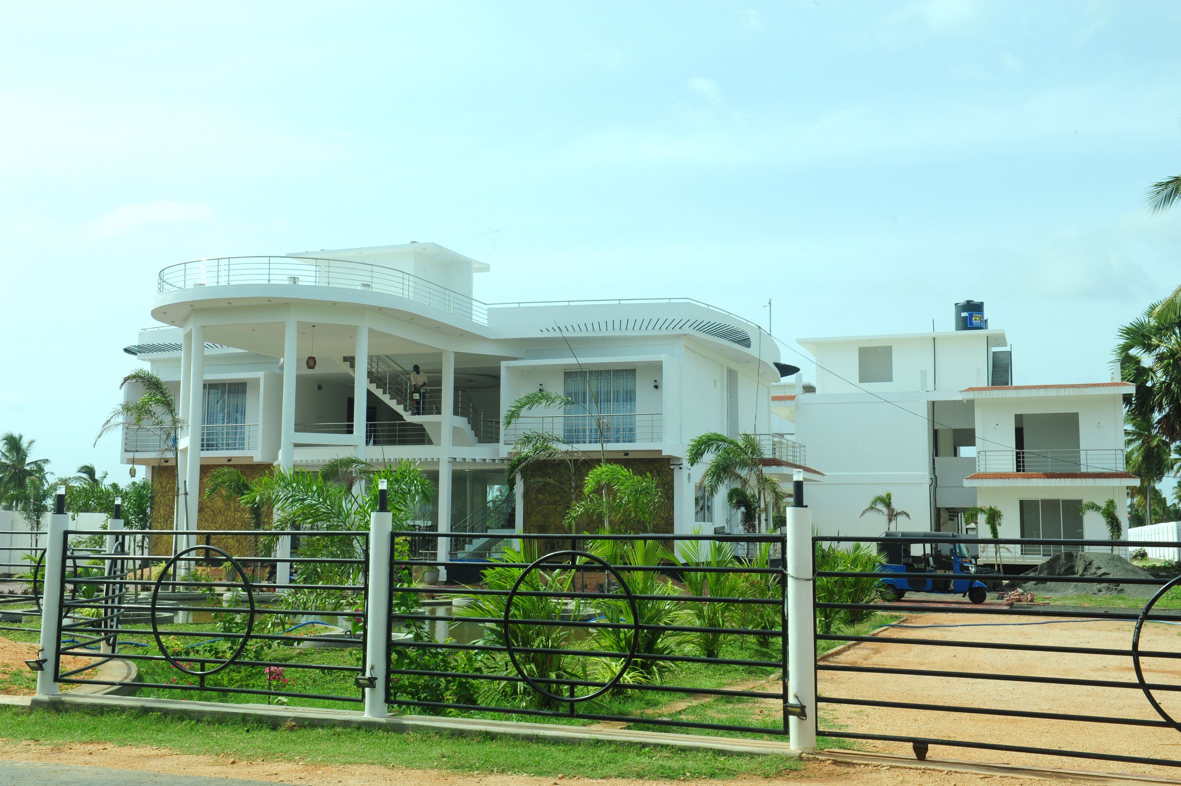 A modern multi-story building with balconies, a gated entrance, and surrounding greenery.
