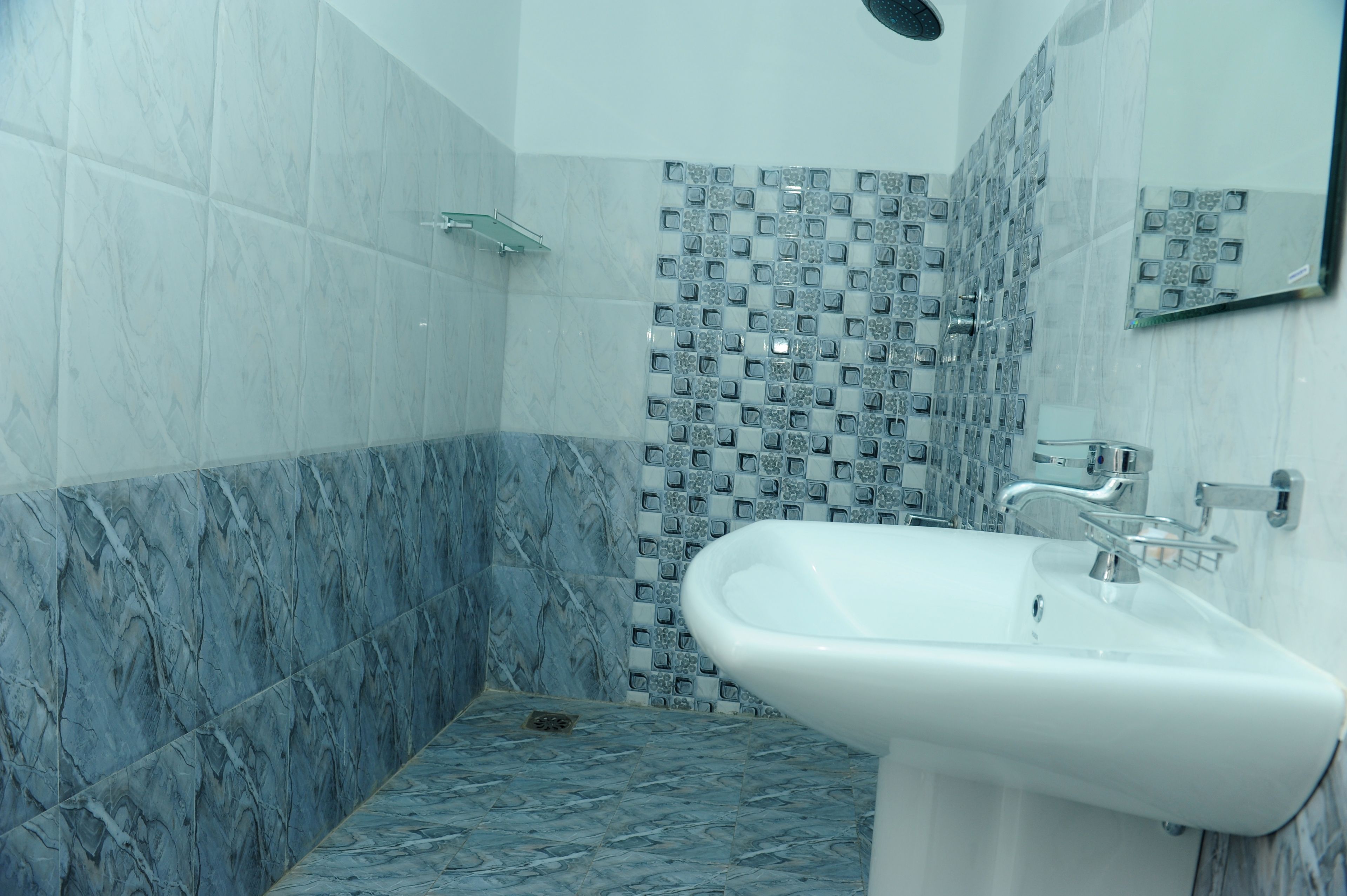 A bathroom with a marble floor, a sink, and a shower area with patterned tiles.