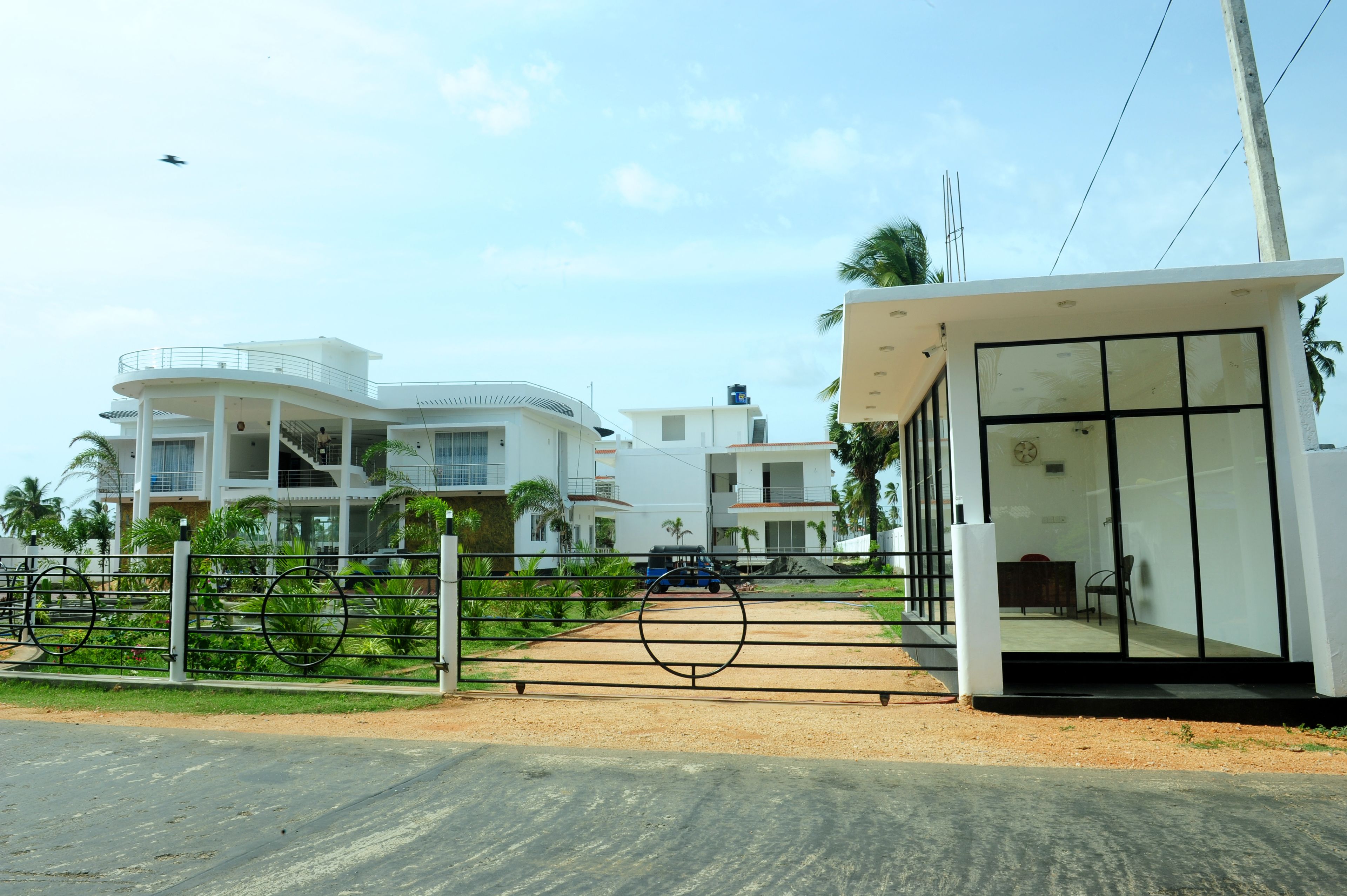 A modern residential building with a gated entrance, a covered waiting area, and a vehicle parked in the driveway.