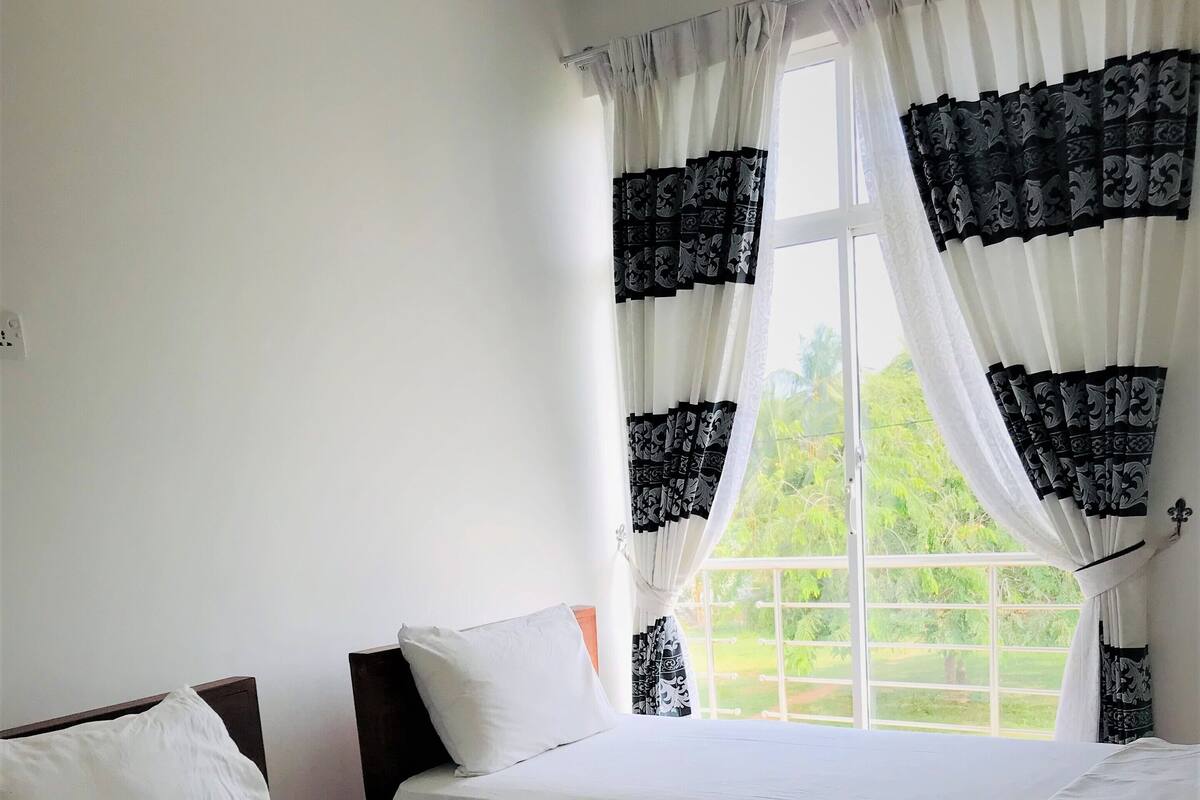 Habitación de hotel con dos camas, ropa de cama blanca y una ventana con cortinas blanco y negro.