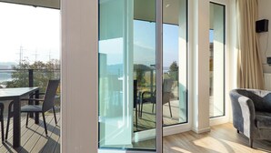 Ein modernes Wohnzimmer mit einer Glasschiebetür, die auf einen Balkon mit Blick auf das Meer und entfernte Schiffe führt.