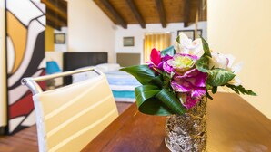 A dining table with a vase of flowers, a striped chair, and a bed in the background.