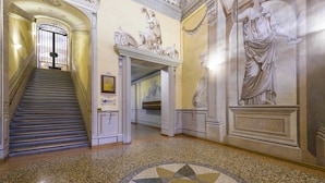 A grand hallway with a marble floor, a staircase, and classical wall art.