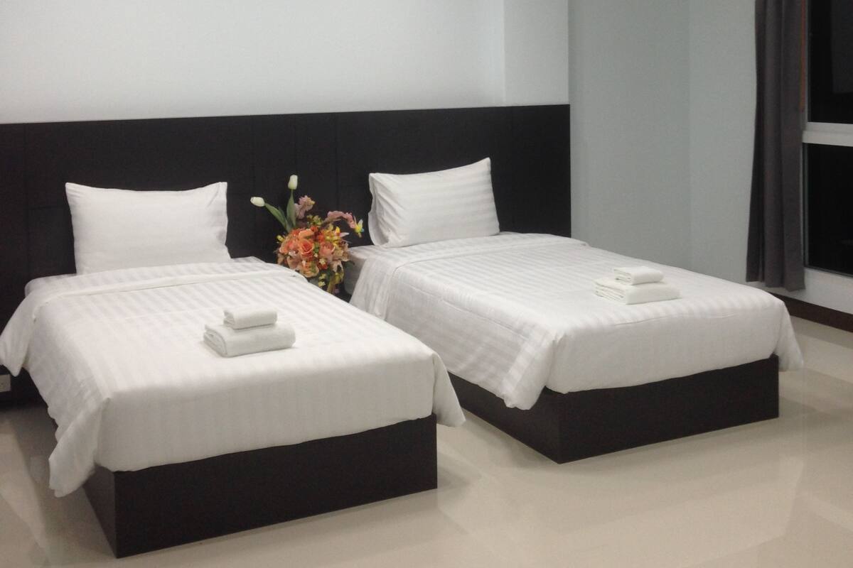 A hotel room with two beds, a dark headboard, a flat-screen TV, and a window with curtains.