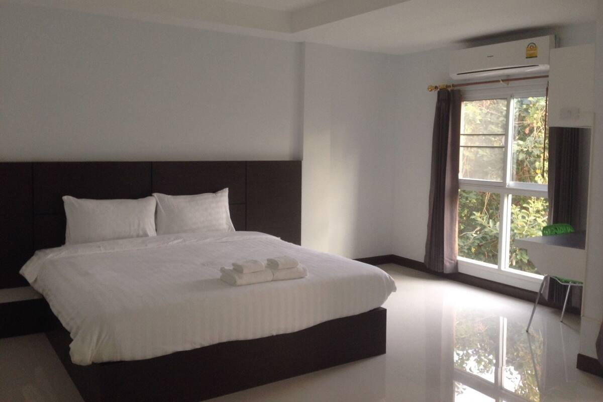 A modern bedroom with a large bed, a dark headboard, and a window with curtains.
